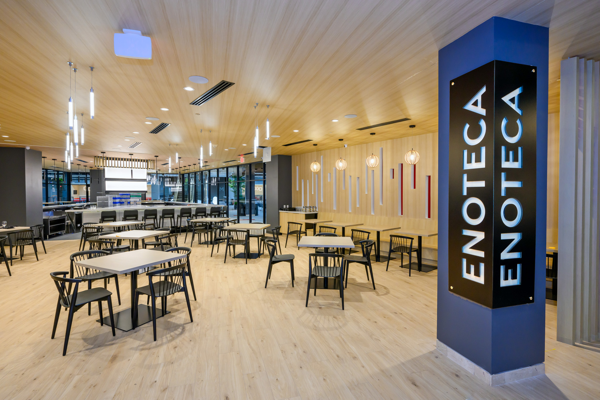 A modern, spacious restaurant with wooden floors, minimalist decor, and tables neatly arranged; a sign reads "ENOTECA" on a pillar.