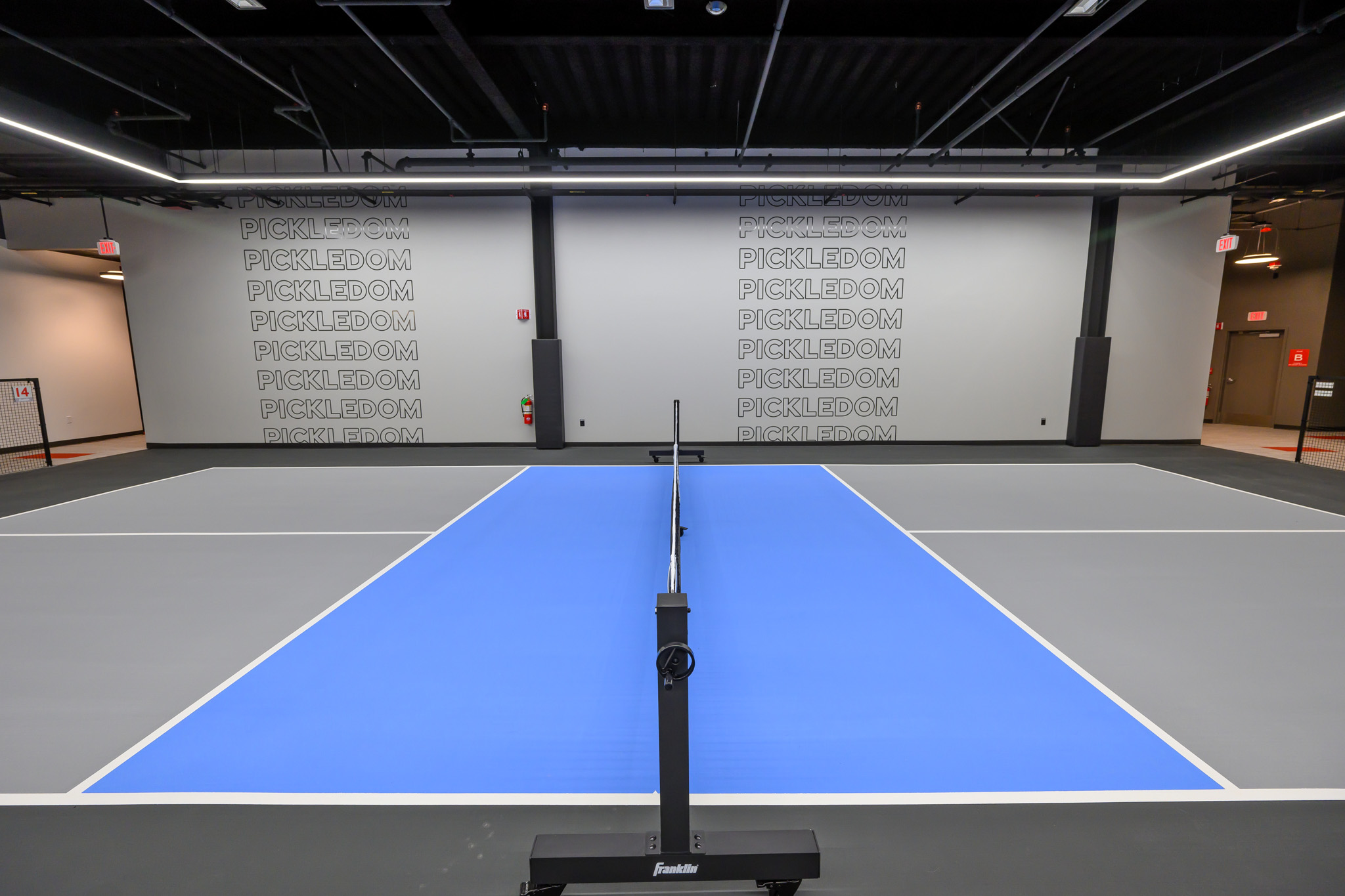 An indoor pickleball court with a blue playing surface, gray surroundings, and