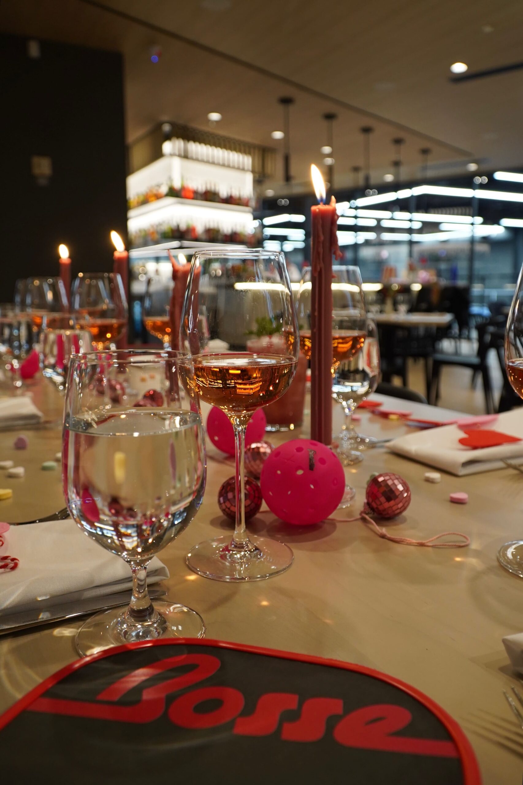 Candlelit dining table set with glasses of rosé, water, and festive pink decorations, creating a cozy and vibrant ambiance at the Bosse venue.