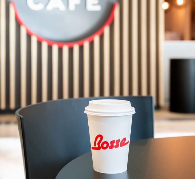 Cup of hot coffee from Bosse Café on a round table with branded wall logo in the background