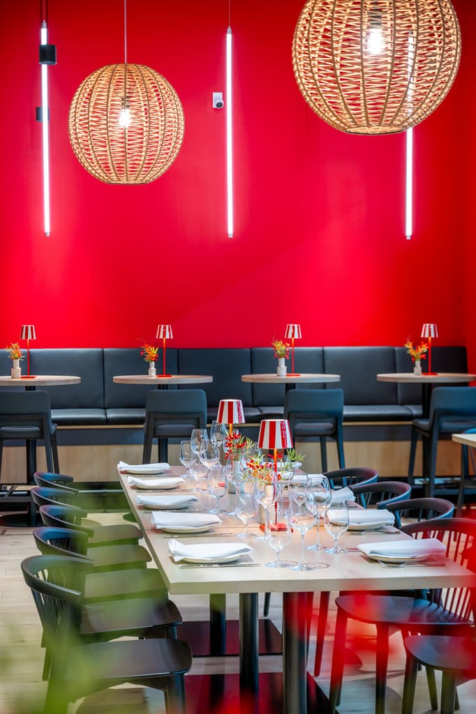Long table setting at Enoteca with glowing pendant lights and red wall in background.
