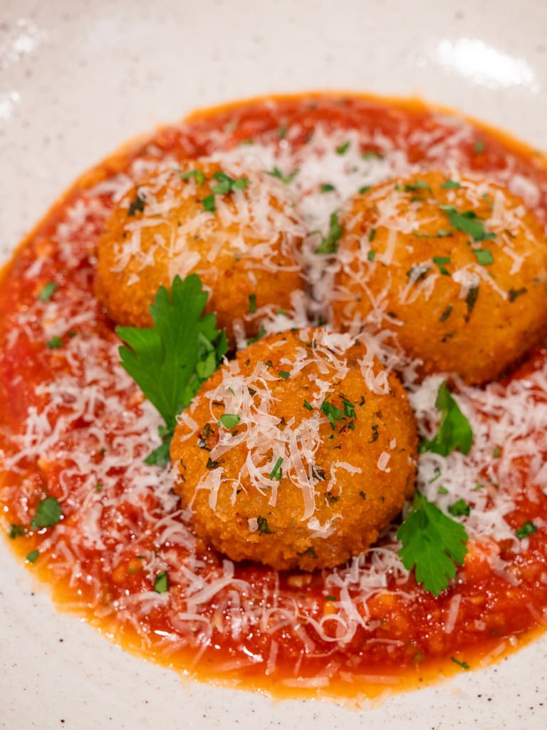 Arancini balls topped with grated cheese on a bed of tomato sauce.