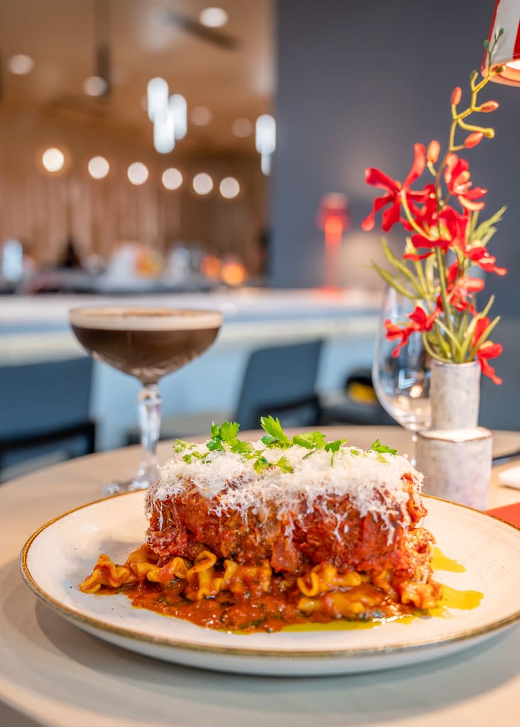 Rich lasagna topped with parmesan cheese served with an espresso martini and wine glass