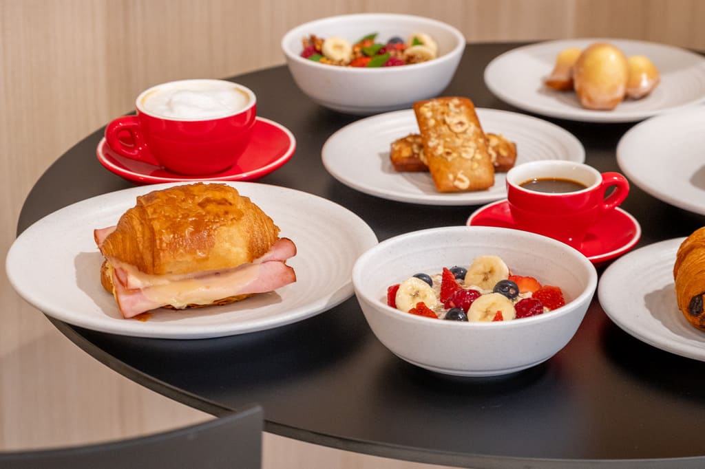 Croissant sandwich, fruit bowls, and coffee on round black table