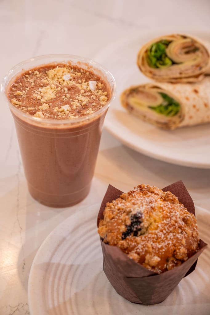 Chocolate smoothie, muffin, and wrap sandwich on white plates