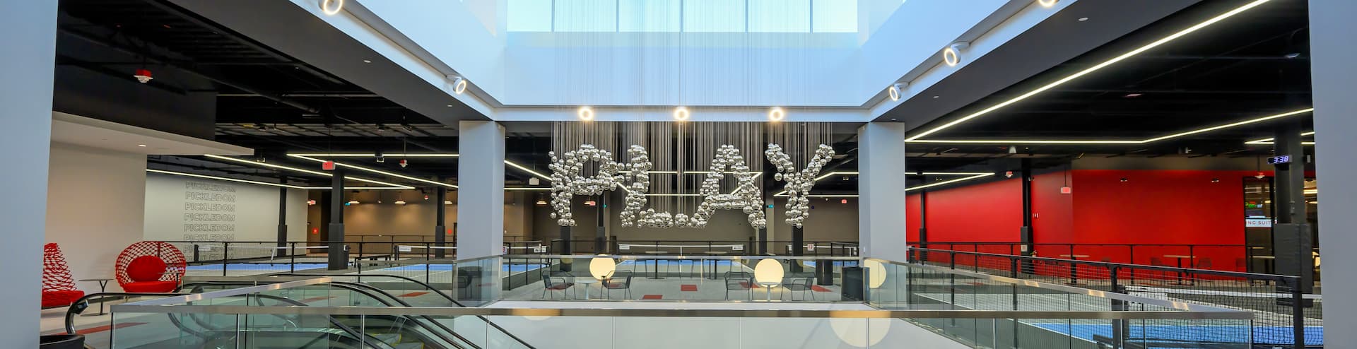 Modern indoor BOSSE Pickledom space featuring pickleball courts, escalators, seating areas, and a large PLAY installation.